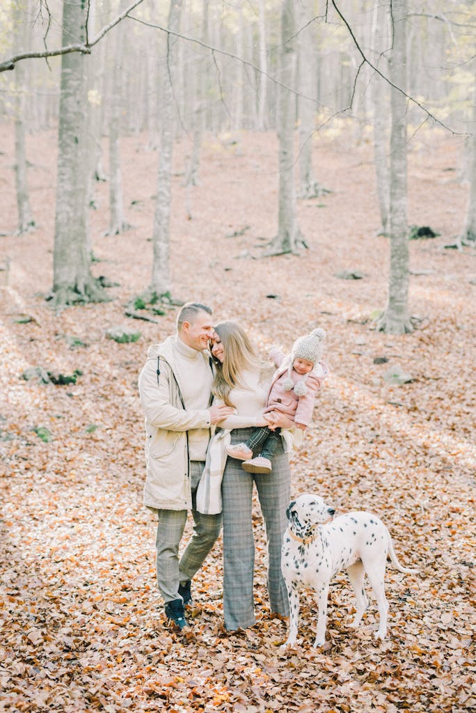 A happy family strolls with their Dalmatian in a beautiful fall forest setting.