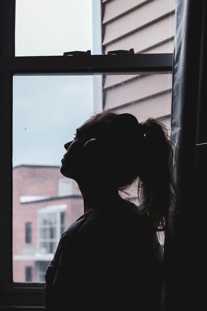 A silhouette of a woman wearing headphones, deep in thought by a window.