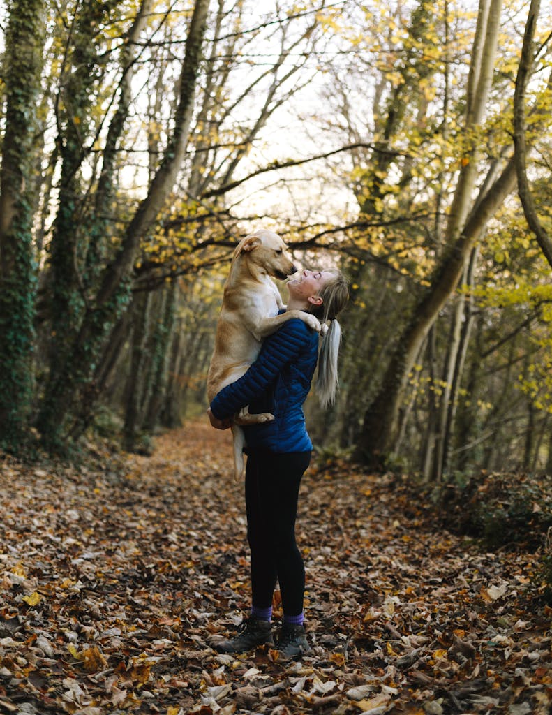 A woman holding her dog amidst a colorful fall forest path, expressing joy and affection.