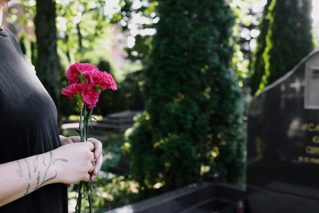 A woman holding pink flowers at a cemetery, symbolizing remembrance and affection.