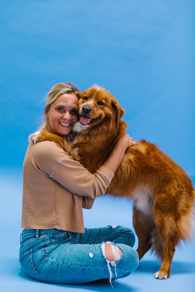 A woman joyfully hugs her golden retriever on a vibrant blue backdrop.