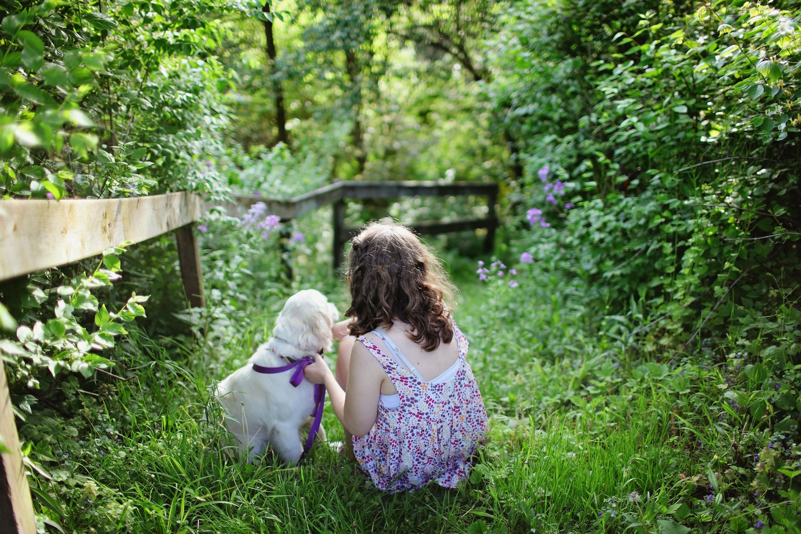 A young girl with her puppy in a vibrant green garden, enjoying a sunny summer day.