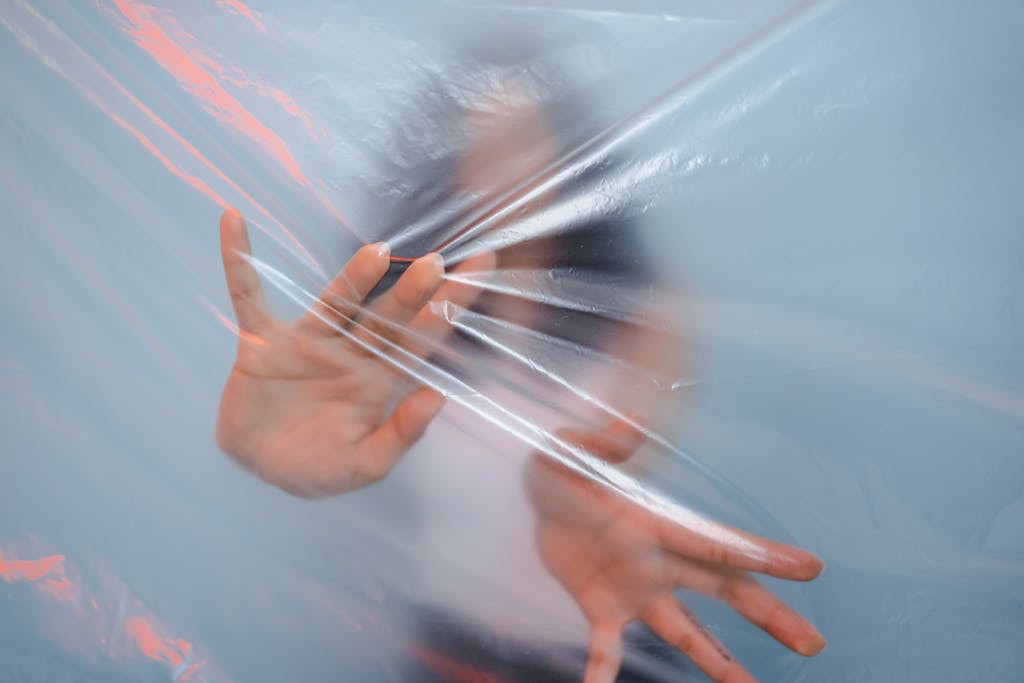 Blurred individual reaching through plastic, symbolizing environmental concerns and barrier themes.