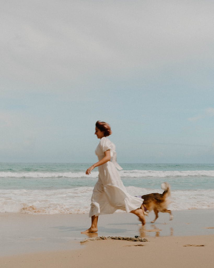 Carefree woman running with her dog along a sunny beach in Phuket, Thailand, embracing summer joy.