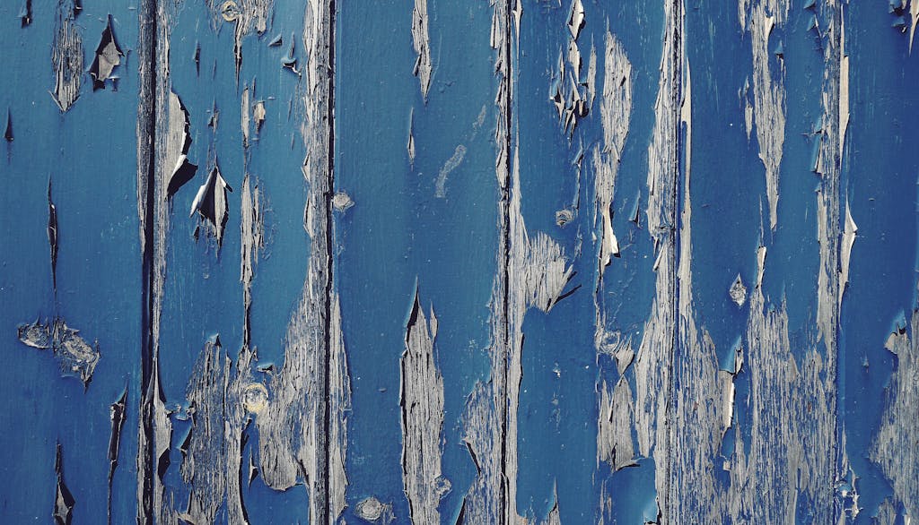 Close-up of a blue painted weathered wooden wall with peeling paint texture.