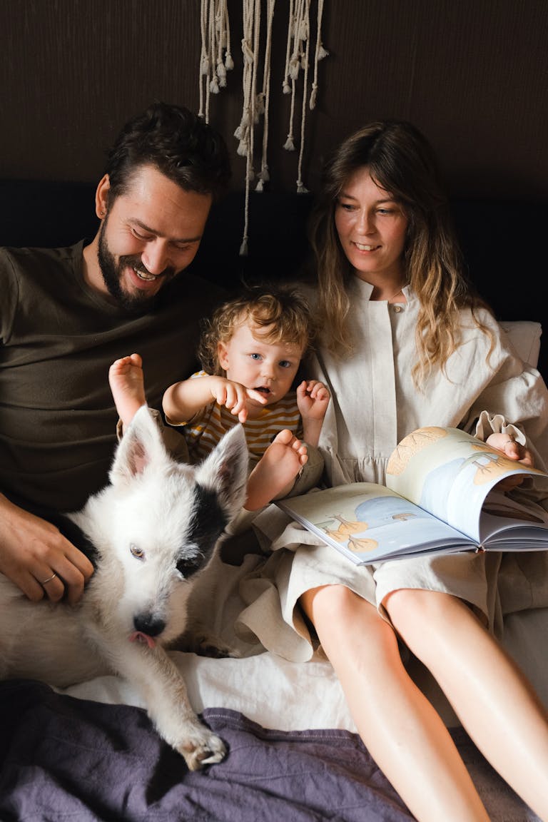 Family enjoying quality time with their dog and a book in a cozy bedroom setting.