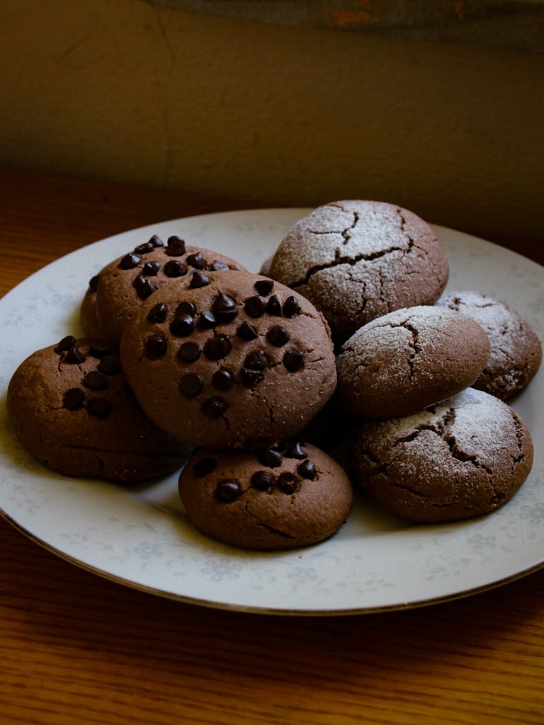 Freshly baked chocolate chip cookies with powdered sugar on a decorative plate.