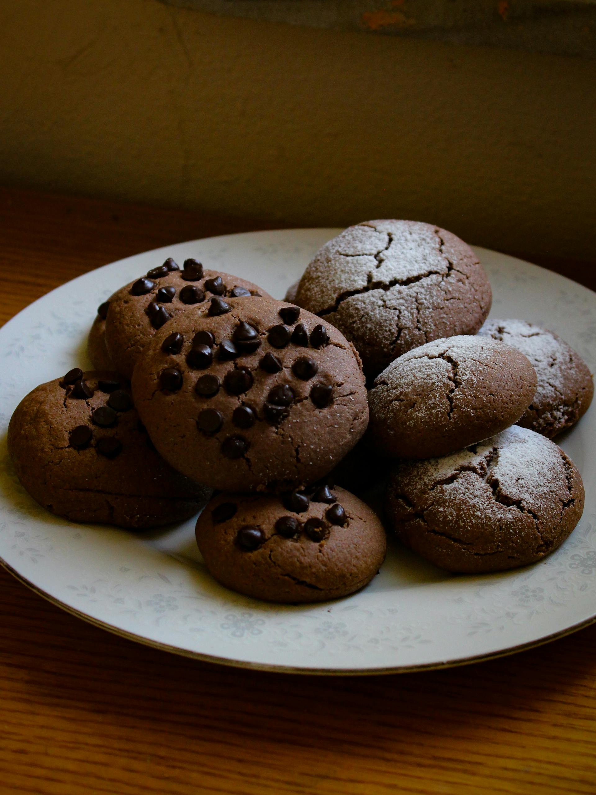 Freshly baked chocolate chip cookies with powdered sugar on a decorative plate.