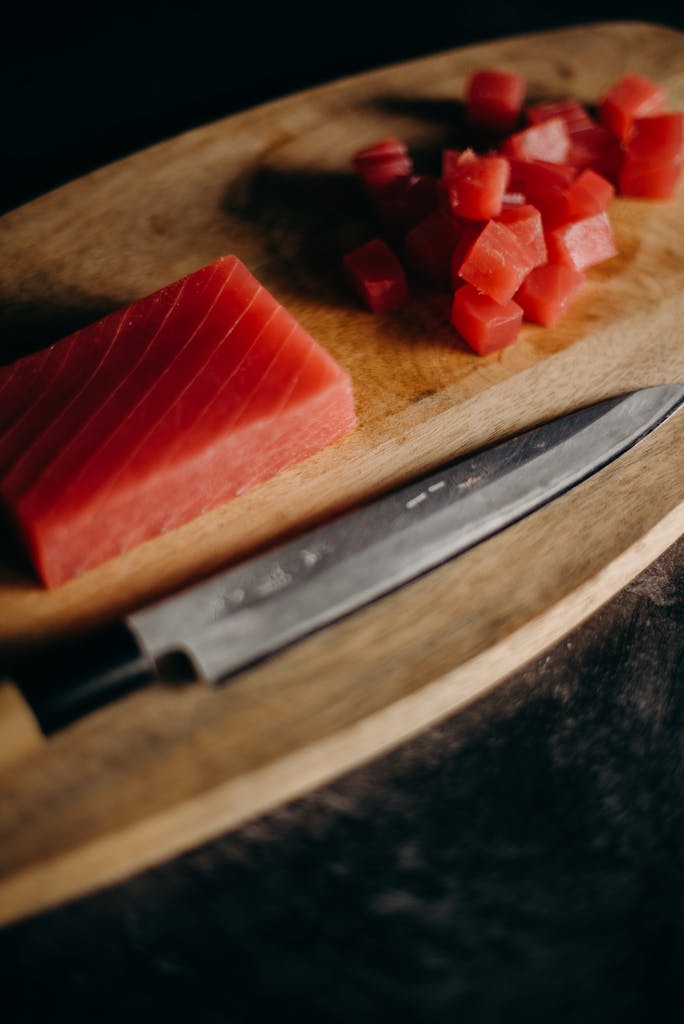 Freshly sliced tuna on a wooden chopping board with a sharp knife, perfect for Asian cuisine preparations.