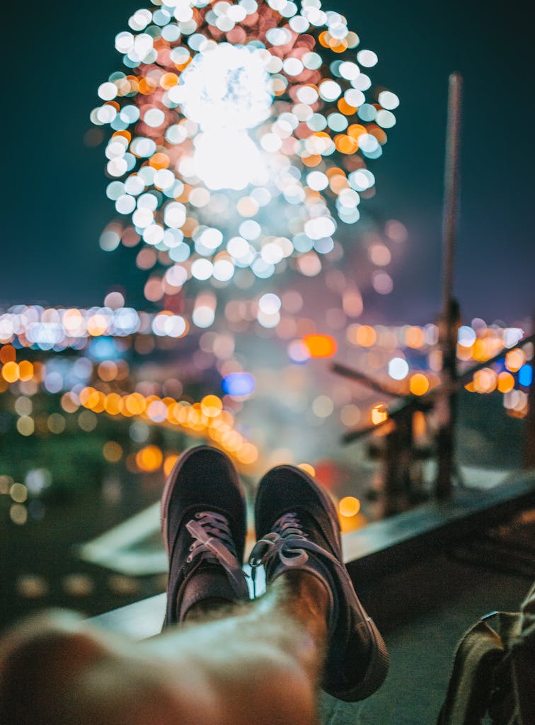 Person enjoying a rooftop view of vibrant fireworks in Minneapolis at night.
