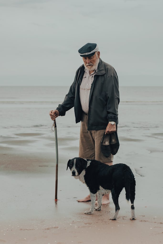 Senior man with cane and dog at a peaceful beach, embodying companionship and leisure.